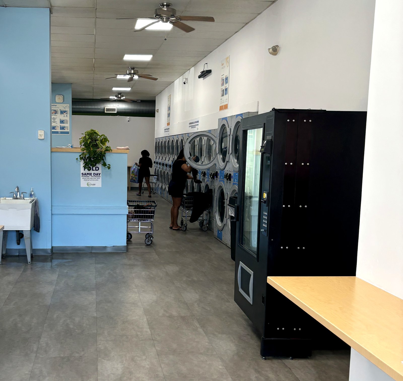 The bright, newly renovated interior of Scrubs Laundry in Chelsea — a long, open aisle with rows of machines and folding space