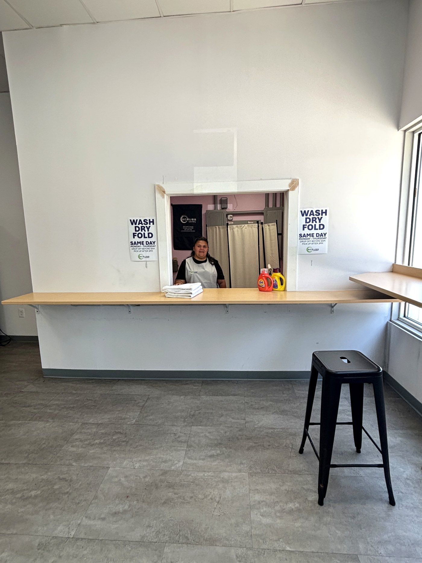 A Scrubs Laundry attendant at the wash & fold drop-off window with freshly folded laundry